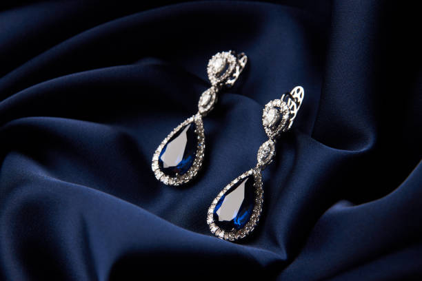 wo Golden sapphire earrings with small diamonds. Pair of platinum earring with sapphire gemstone on blue satin background. Luxury female jewelry, close-up